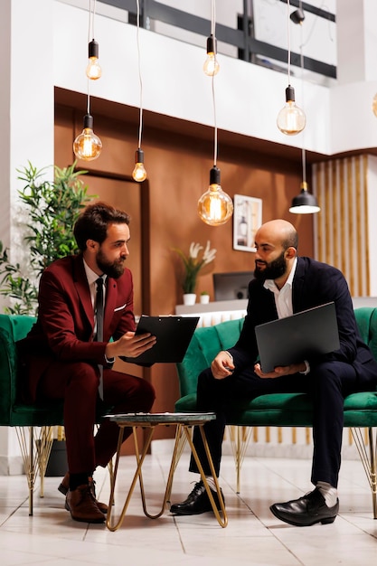 Corporate team reviewing project ideas at international meeting in hotel lounge area, discussing with colleague at business conference. Entrepreneurs travelling for work at resort.