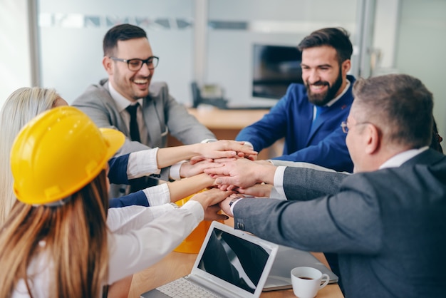 Corporate team stacking hands while sitting at desk at boardroom. Replace the fear of the unknown with curiosity.