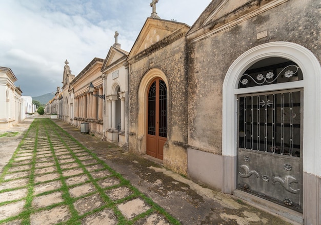 Corridor in a cemetery with tombs on the sides below cloudy sky