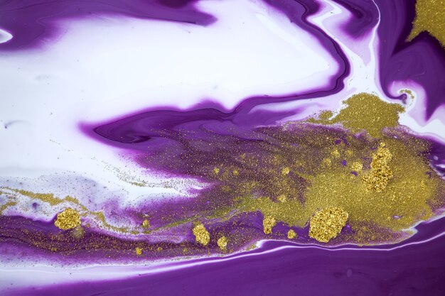 Cose up gold glitter on liquid mixed purple inks background.