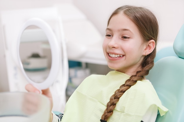 Cose up of a lovely girl looking in the mirror, checing her teeth fter dental treatment