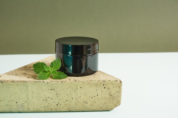 Cosmetic black cream jar and fresh mint on triangular stone light blue background. Organic cosmetics concept. Natural cosmetic product concept. skin care product with peppermint oil