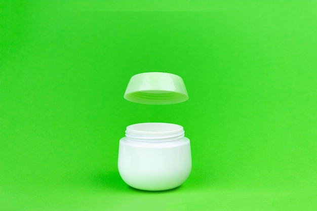 Cosmetic bottle for cream. beauty cream container with open lid cup on green.