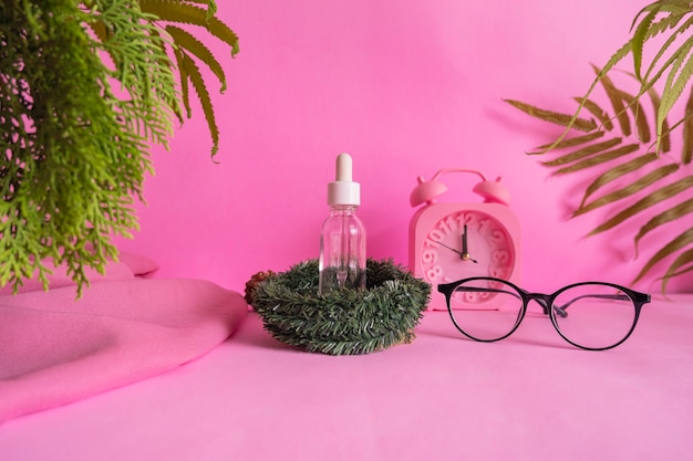 Cosmetic bottle minimalist concept idea on pink background with alarm clock decoration, leaves and glasses