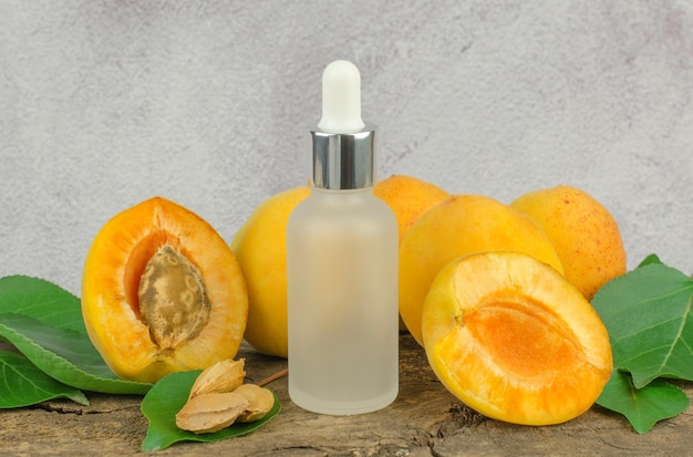 Cosmetic bottle with apricot essential oil and fresh apricot fruit on a wooden table Essential oil of apricot and apricot kernels