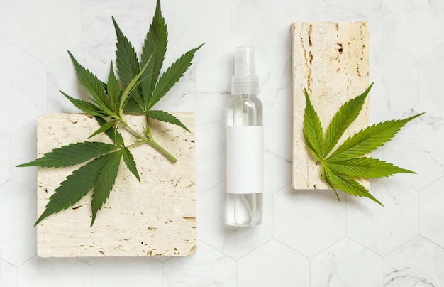 Cosmetic bottle with blank label near green cannabis leaves and beige stones top view mockup