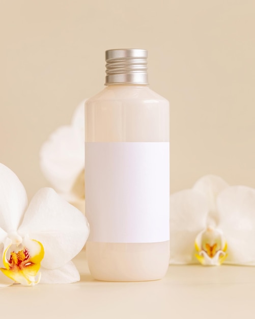 Cosmetic bottle with blank label near white orchid flowers on light yellow Mockup