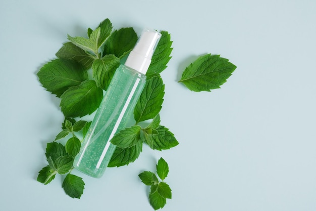 Bottiglia cosmetica con gel verde e menta fresca su sfondo blu pietra triangolare. prodotto per la cura della pelle con olio di menta piperita