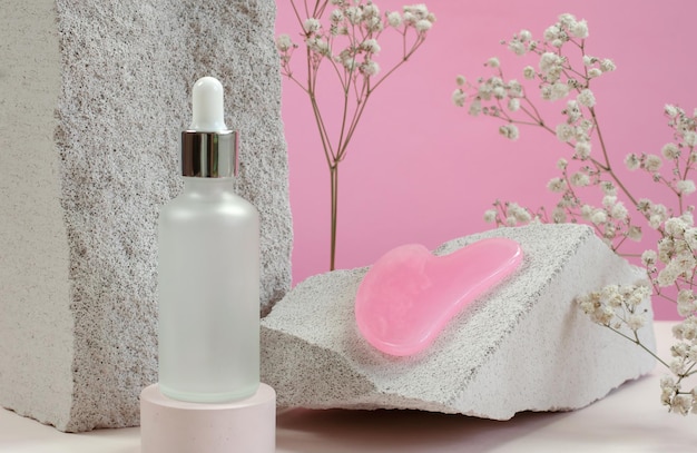 Photo cosmetic bottle with serum or essential oil scraper for facial massage on the background of natural stones and gypsophila