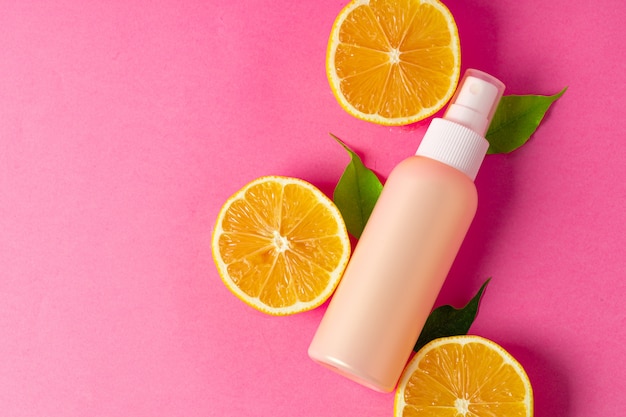 Cosmetic bottle with sliced citrus fruits on bright pink