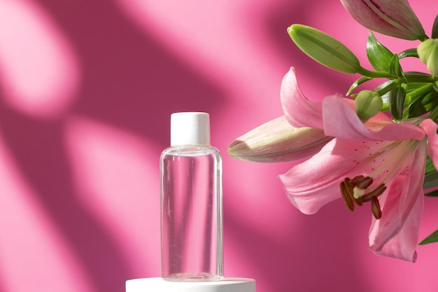Cosmetic bottle with tonic water on podium with lily flower and shadow on pink background Face and body care spa concept Hyaluronic acid oil serum with collagen and peptides skin care product