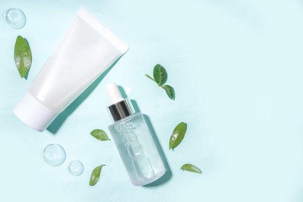 Cosmetic bottle with water drops, bubbles  and green leaves. Moisturizing, Facial Care, reparing and skincare product.  Top view flaylay copy space