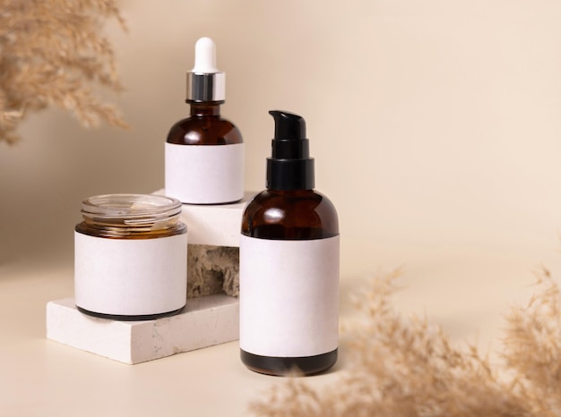 Photo cosmetic bottles on beige stones near dry pampas grass on light beige close up labels mockup