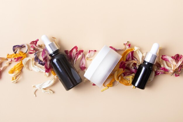 Cosmetic bottles and jar with dry colored flower petals on a beige background top view