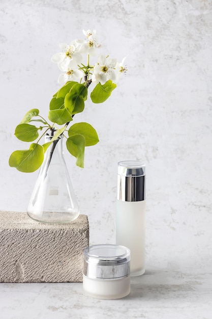 Cosmetic bottles laboratory flask and a sprig of blooming pear on a gray background