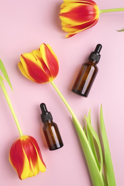 Cosmetic bottles made of amber glass and tulips on a pink background The concept of natural cosmetics and minimalistic packaging The concept of skin care