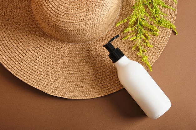 Cosmetic bottles and straw hat on brown background