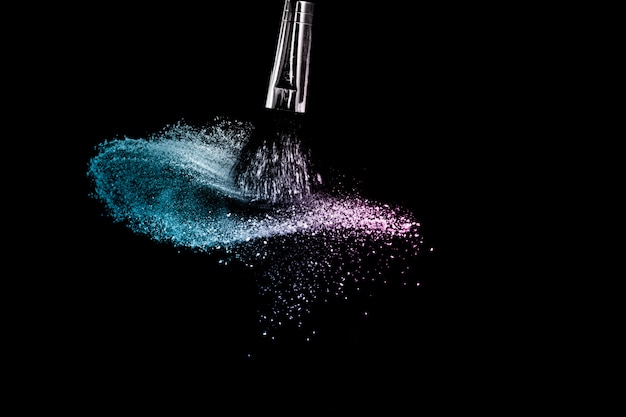 Foto spazzola cosmetica con polvere cosmetica dell'oceano viola e blu che si sparge per il truccatore o la progettazione grafica nel fondo nero