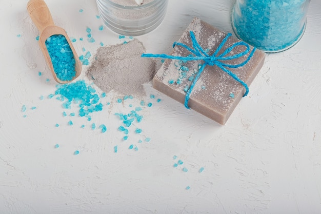 Cosmetic clay powder, homemade clay soap and blue bath sea salt on white background. Face care, body care and spa concept.