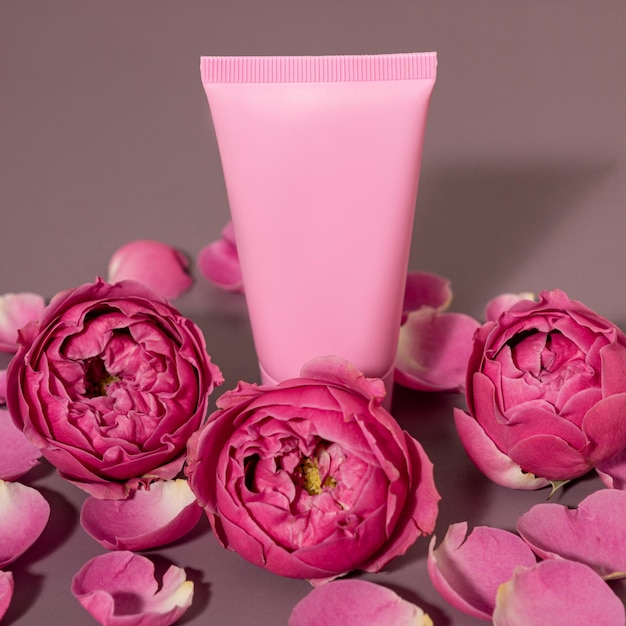 Cosmetic container mock-ups, cream tube on pink floral background with roses. close up, copy space, background.