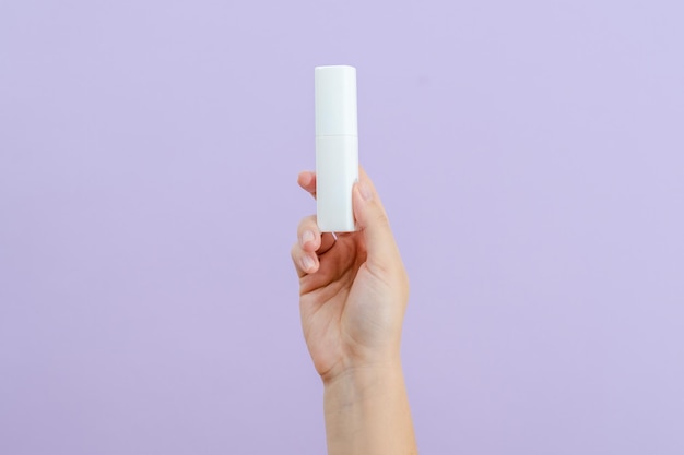 Cosmetic cream battle in womans hand on light lilac background\
beauty concept packaging tube for cosmetic products