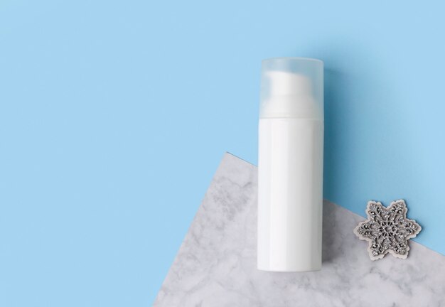 Cosmetic cream in a bottle with snowflake on blue creative table