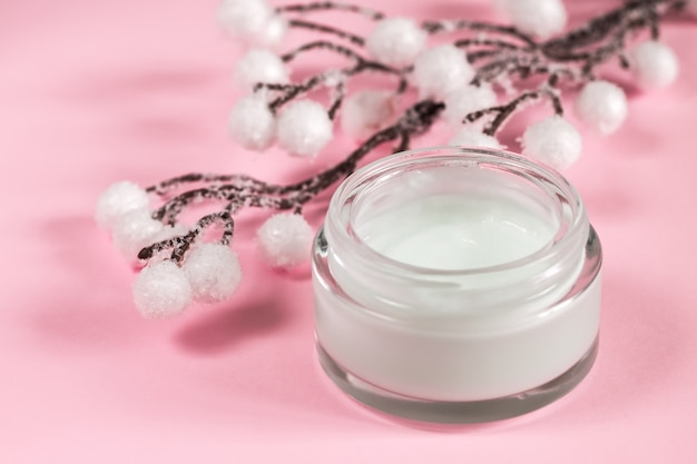 Contenitore cosmetico crema su sfondo rosa con fiori.