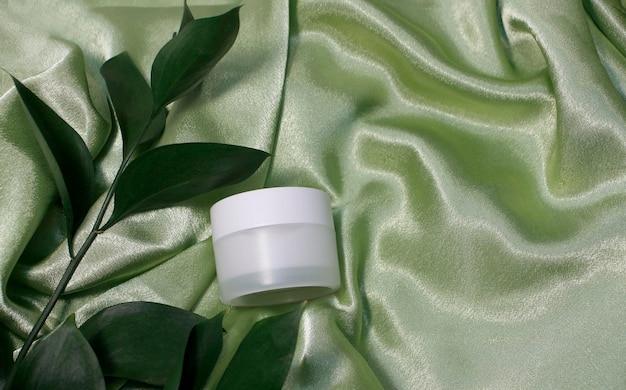 Cosmetic cream facial mockup tube container or body lotion, green leaves. Natural cosmetic product concept, top view, copy space.