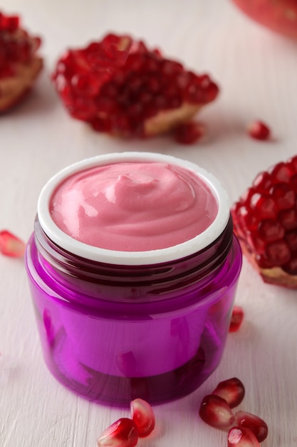 Cosmetic cream in a lilac jar and with fresh pomegranate on a white wooden table.