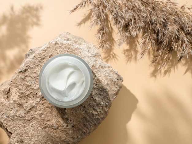 Photo cosmetic cream or moustirizer on stone pampas grass on pastel beige background beautiful shadows open round glass jar with aesthetic swirls face cream top view or flat lay copy space