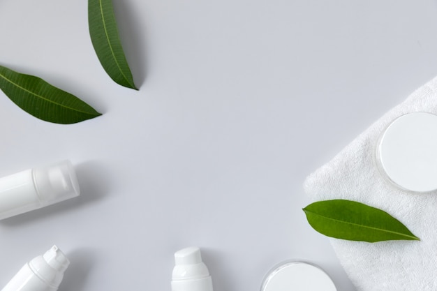 Cosmetic cream, towel and leaves on white background