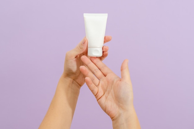 Cosmetic cream tube in womans hand on lilac background Beauty concept Packaging tube for cosmetic productsxA