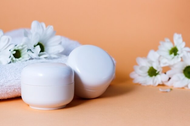 cosmetic cream in white tubes or bottles on a beige background with white flowers