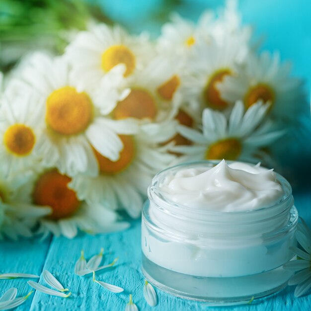 Cosmetic cream with camomile flower or a body and face on blue wooden table