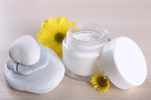 Cosmetic cream with flowers and spa stones on wooden background