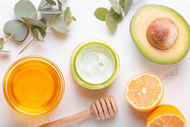 Crema cosmetica con ingredienti biologici naturali miele di avocado limone ed eucalipto foglie su sfondo di pietra bianca cosmetici e cura della pelle organica per il concetto di prodotto per la cura del viso e del corpo flat lay xa