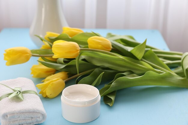 Cosmetic cream and yellow tulips on the table