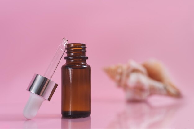 A cosmetic dropper bottle and sea shell on the pink background