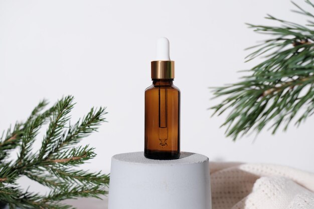 cosmetic face essential oil in amber glass bottle with dropper oil standing on a grey cement podium next to pine branch christmas sale concept