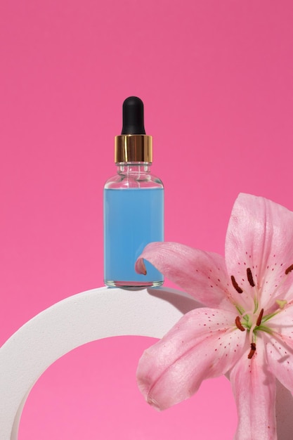 Cosmetic glass bottle with dropper for essential oils and serum on a podium with lily flower face and body care spa concept and natural cosmetics