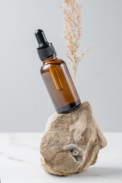 Cosmetic glass bottle with dropper for essential oils and serum on a stone with dry pampas grass