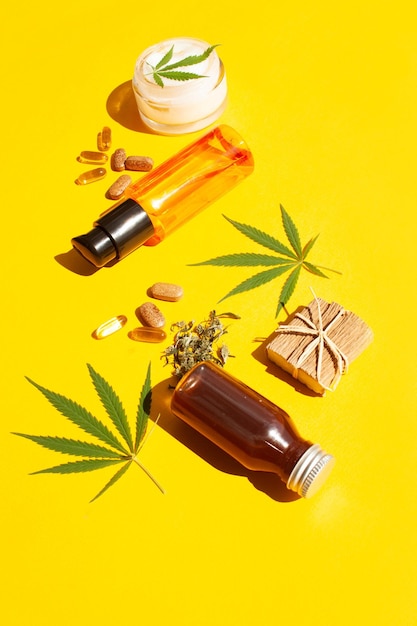 Фото Косметическое конопляное масло, таблетки и натуральный крем на желтом фоне. уход за телом и здоровьем