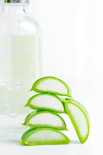 Foto lozione cosmetica fatta in casa o olio essenziale dalla pianta naturale a fette di aloe vera in bottiglie di vetro contro grigio chiaro.