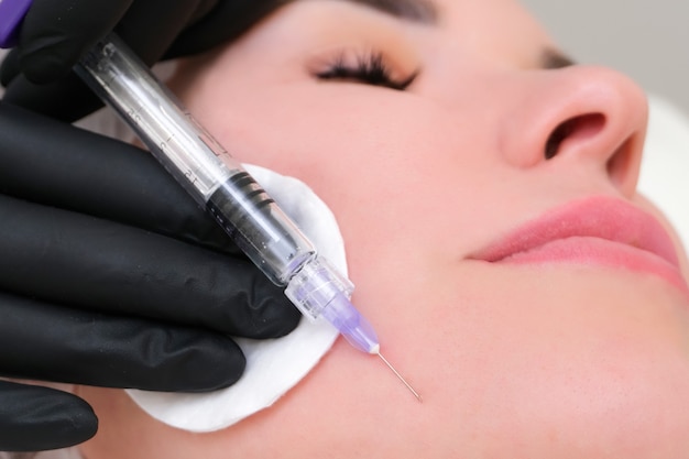 Photo cosmetic injections for skin rejuvenation. cosmetologist injects a syringe into the skin of a young woman.