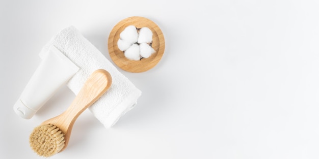 Cosmetic layout with cream tube, wooden brush, cotton flower and towel on beige background. Selfcare, home spa and relaxation concept. Flat lay, top view. Banner