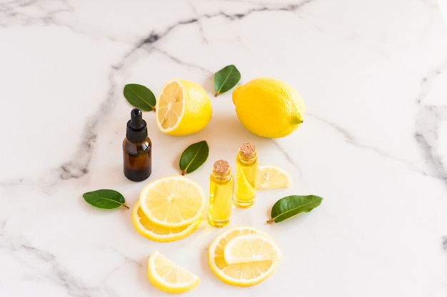 Cosmetic lemon oil and citrus essential oil on a marble table. fruits of fresh lemon and melisa leaves. cosmetics of nature in glass bottles.