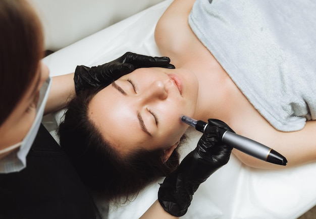 Cosmetic mesotherapy for facial rejuvenation Cosmetic procedure of microneedling The cosmetologist injects hyaluronic acid into the face of the girl's patient with the help of dermopen