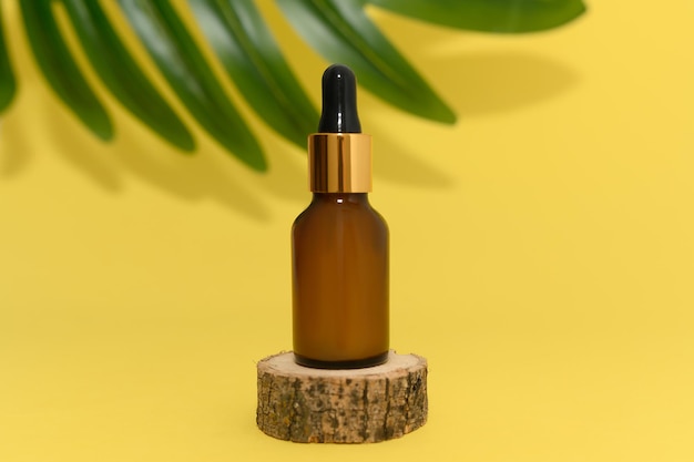 Cosmetic oil in a glass bottle stands on a wooden podium Palm leaf on a yellow background