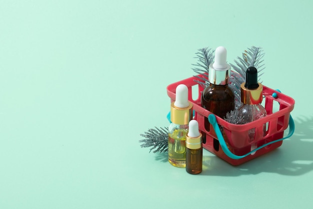 Cosmetic oil and serum bottles with pipette in shopping basket with winter decor on mint background copy space