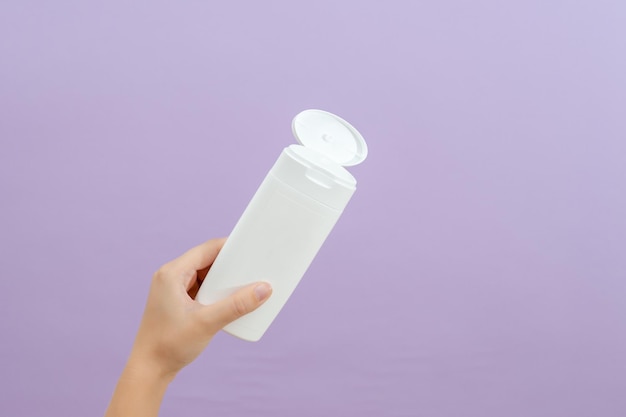 Cosmetic packaging tube in womans hand on lilac background\
beauty concept tube for cosmetic products